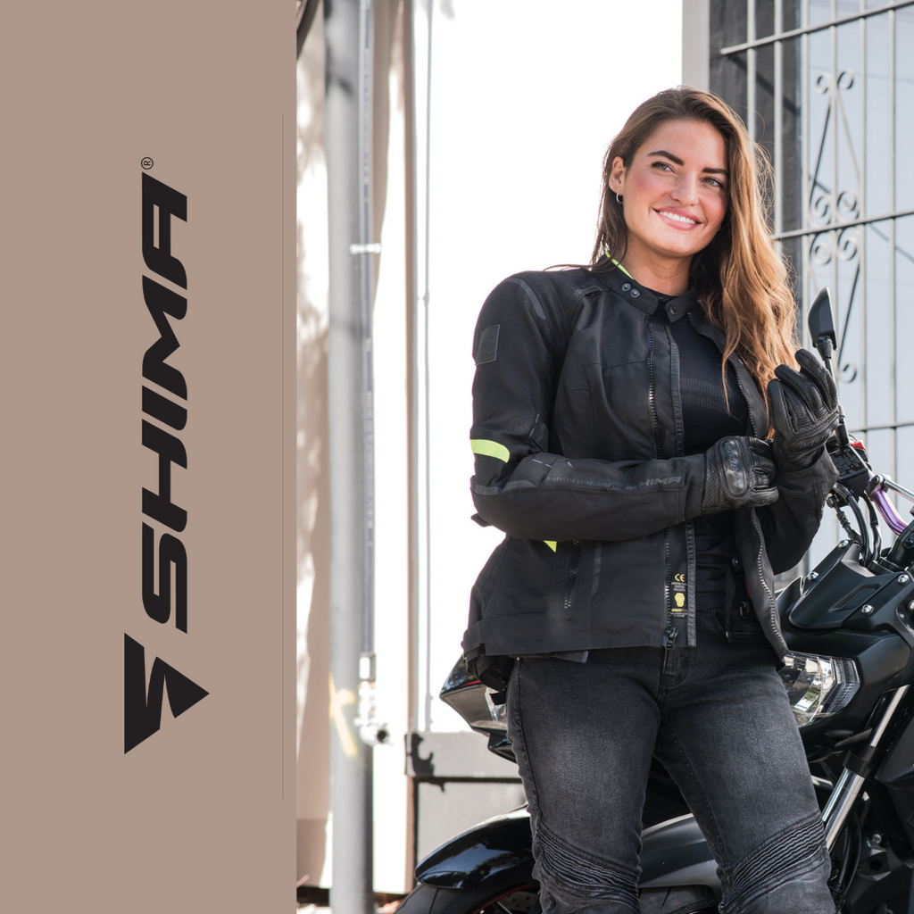 A smiling woman standing by the motorcycle and wearing Shima motorcycle clothes for female