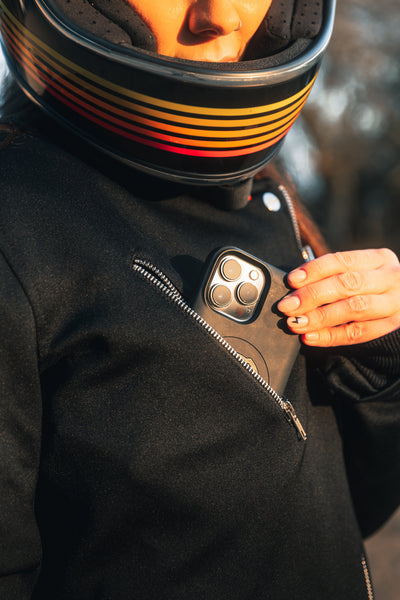 woman pitting her phone in a pocket of a Black retro style woman's motorcycle jacket with silver zip details