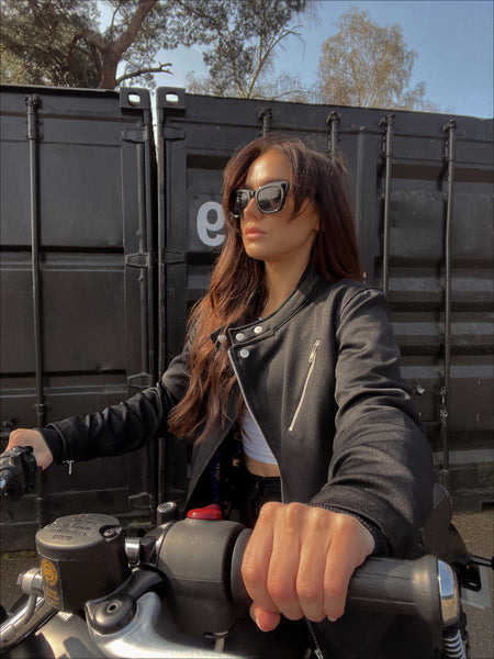 a young lady on a motorcycle wearing Black retro style woman's motorcycle jacket with silver zip details