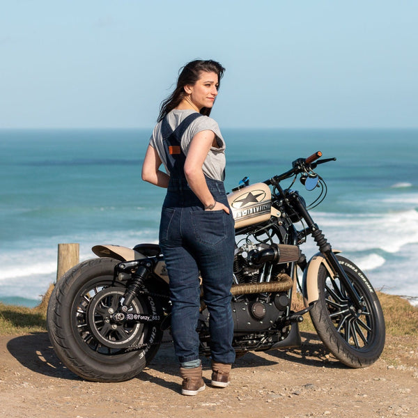 A woman by the beach with her motorcycle wearing blue women's motorcycle overall from Moto Girl