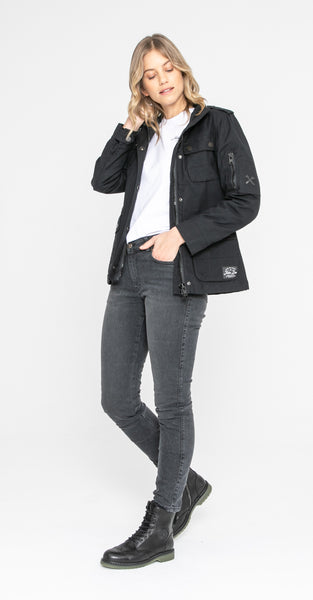 A woman wearing grey jeans and BLACK army style women's motorcycle jacket from John Doe