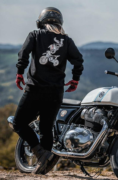 A woman near her motorcycle wearing black motorcycle sweatshirt for women with high neck and drawing on the back