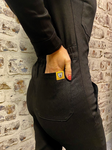 A close up of a woman holding her hand in the back pocket of black women's garage jumpsuit from MotoGirl