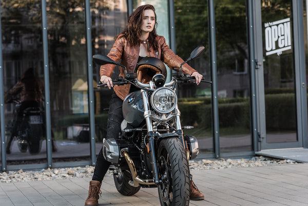 A young woman by a motorcycle wearing brown motorcycle leather jacket and brown women motorcycle boots from Shima