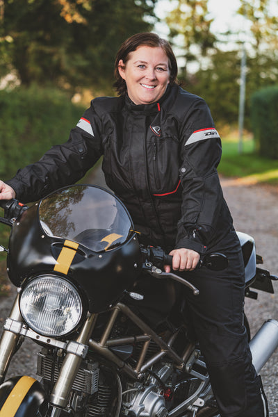 A smiling woman on a motorcycle wearing Difi textile women's motorcycle Nexia jacket and Cyclone pants