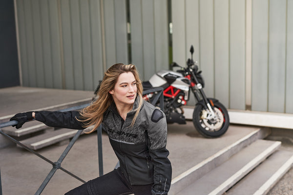 A blond woman near the motorcycle wearing grey women's motorcycle jacket from SHIMA
