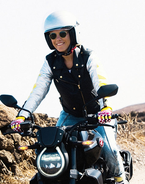 A young happy woman riding a motorcycle and wearing Ride like a Girl pink, black and yellow women's motorcycle gloves from eudoxie