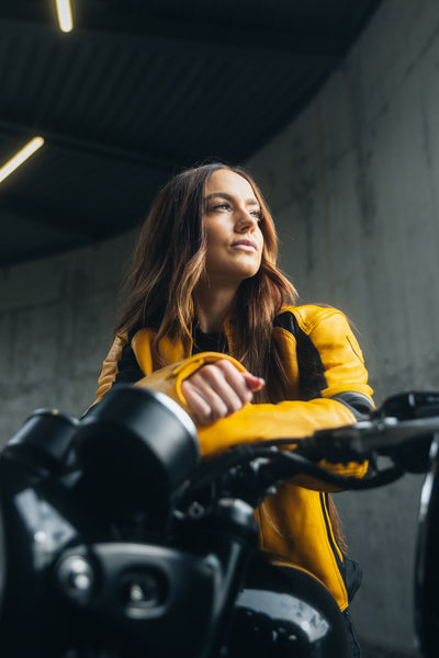 En ung kvinde på sin motorcykel iført en gul motorcykeljakke til damer